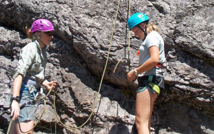 an outward bound student checks their knots while an instructor looks on 